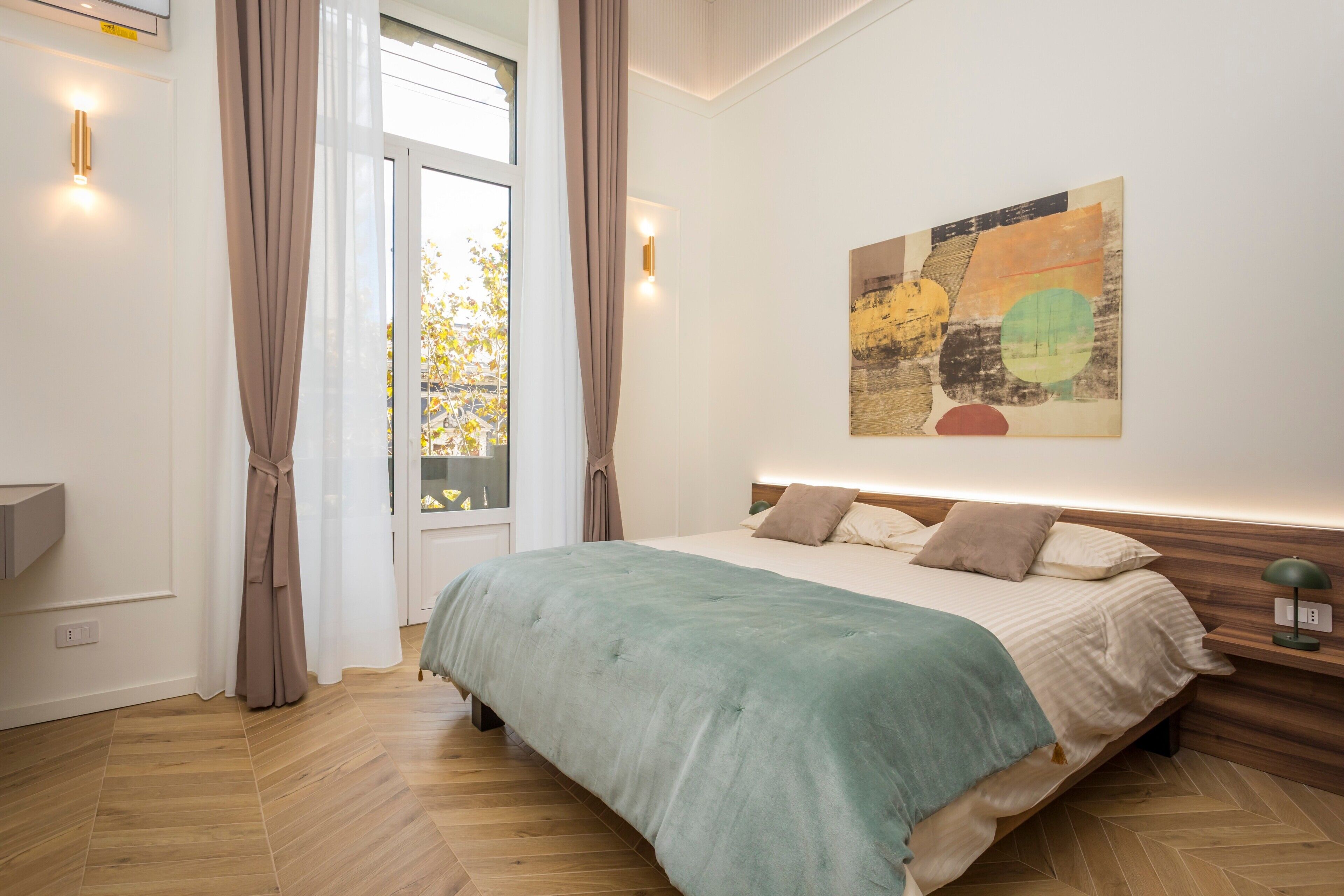A bedroom with a bed, curtains, a wall-mounted artwork, and a window with a view.