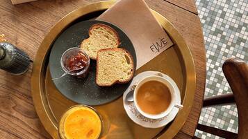 Una mesa redonda de madera con una bandeja que sostiene tostadas, mermelada y una taza de café. Hay una revista sobre la mesa.