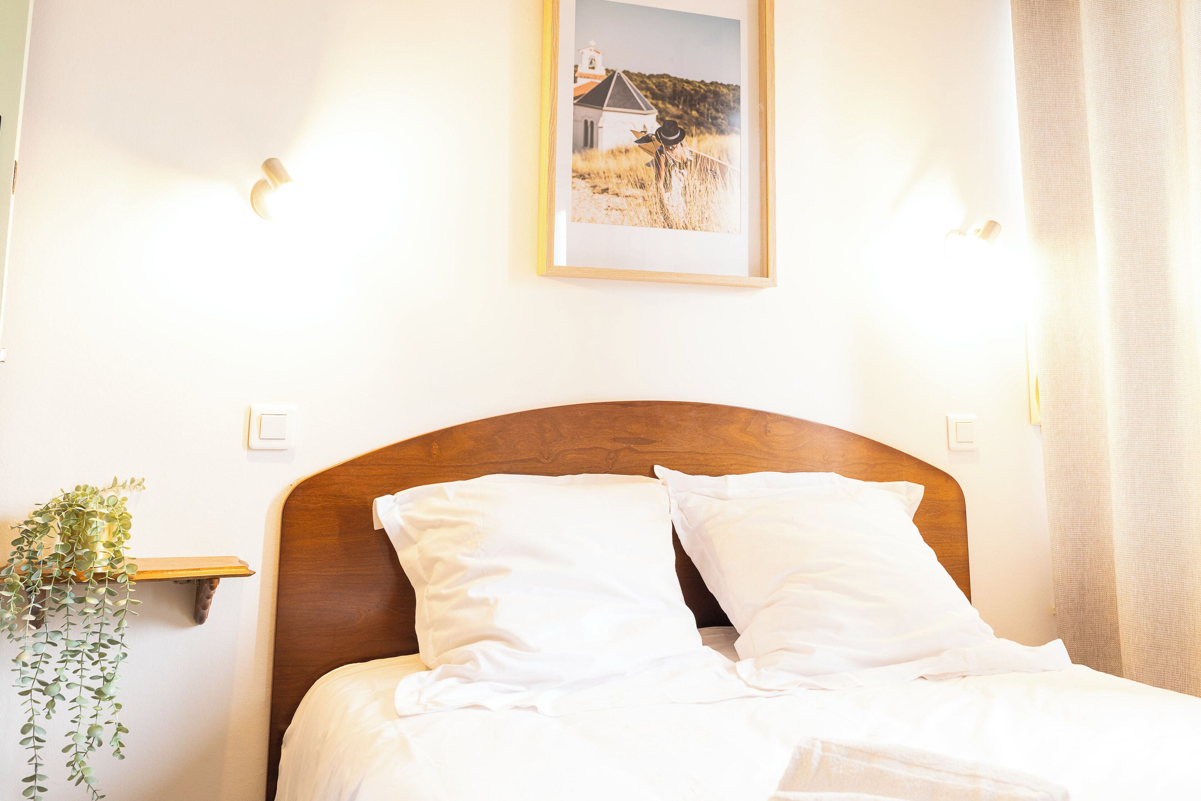 A neatly made bed with white linens, a wooden headboard, and a framed picture above it.