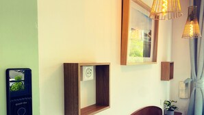 Une chambre d’hôtel moderne équipée d’un lit, d’une table de chevet avec une plante, d’une prise électrique murale, d’un tableau encadré et d’une station de recharge pour téléphone portable.