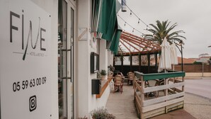 L’extérieur d’un hôtel, avec des places assises en plein air, des plantes en pot et une pergola illuminée de guirlandes lumineuses.