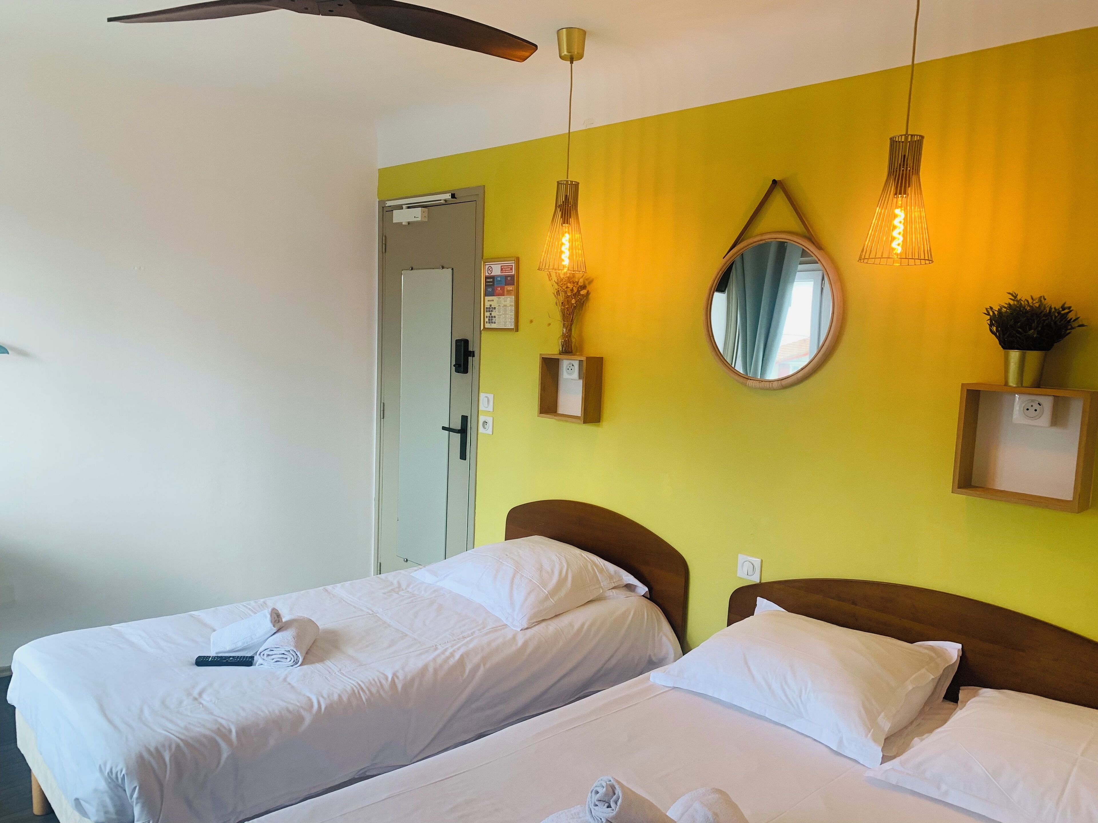 Ein Hotelzimmer mit zwei Betten, einem Deckenventilator, einem Spiegel und Wandleuchten.