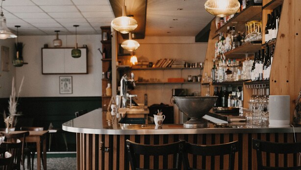 Un espace bar doté d’un comptoir incurvé, de chaises en bois et de luminaires suspendus.