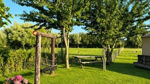 Een gazon met een houten pergola, een picknicktafel en een omheind weidegebied op de achtergrond.
