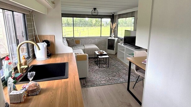 Een moderne keuken met een houten aanrecht, een inbouwfornuis en een spoelbak. Er is een zithoek met een tafel en stoelen, en een groot raam met uitzicht op de omgeving.