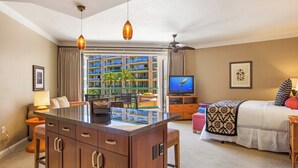 A hotel room with a large window, a TV, a bed, a desk, and a balcony with a view of other buildings. - Honua Kai | Ocean View 4 BR, Sleeps 16 | Car Incl. w/ 6+ Nights | HKH ML-1730 by KBM (Lahaina)