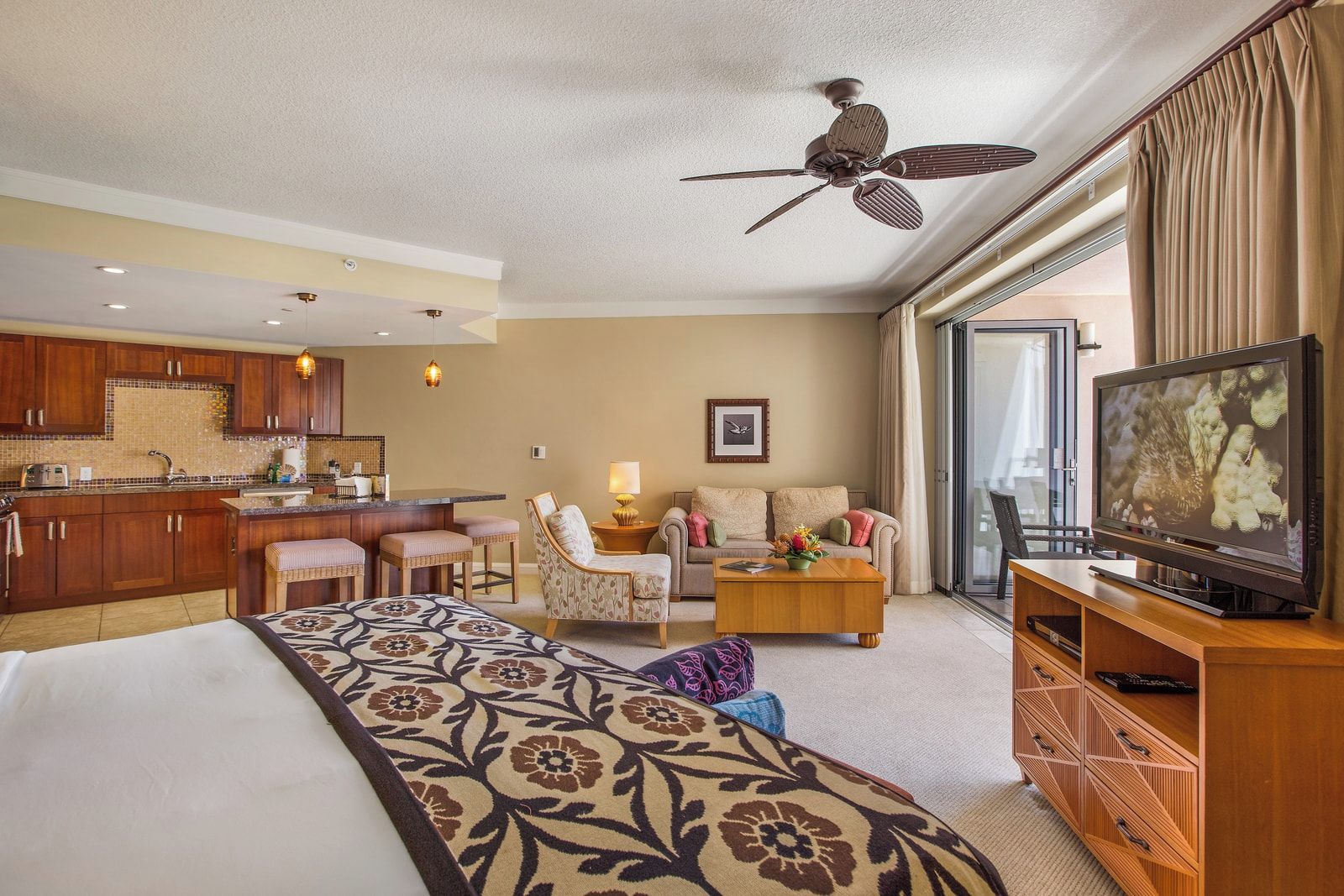 A hotel room with a bed, a television, a dining area, and a kitchenette.