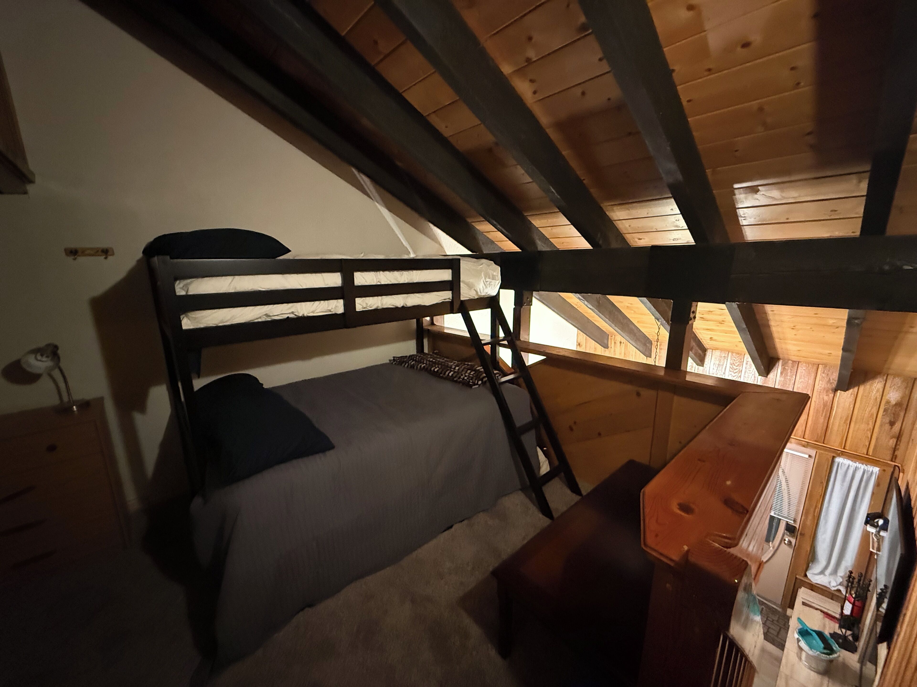 A bunk bed with a desk and chair, wooden beams, and a window in a rustic cabin.