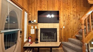 A wooden interior with a fireplace, a TV mounted above it, a staircase, and a door with blinds. - Walk to Giant Steps •1BR+Loft • Fireplace• Fast Wi-Fi• Sleeps 6 •Mountain Views (Brian Head)