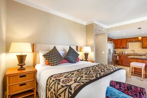 Une chambre d’hôtel avec un lit, deux lampes de chevet, une table de chevet, un plaid à motifs et un petit tabouret.