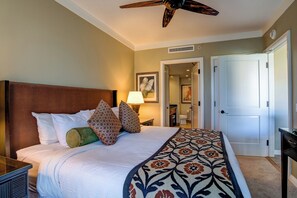 Une chambre d’hôtel comprenant un lit, un ventilateur de plafond, une table de chevet, une lampe et une porte donnant sur une autre pièce.