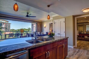 A modern kitchen with a large island, a ceiling fan, pendant lights, and a view of a building outside.