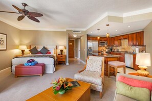 Ein Hotelzimmer mit Bett, Schreibtisch, Stuhl, Couchtisch, einer Küchenzeile und einem Deckenventilator.