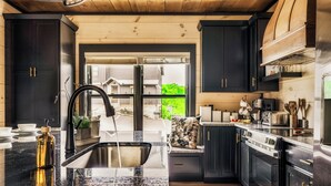 A modern kitchen with dark cabinetry, a granite countertop, and stainless steel appliances. - Star Gazer Luxury Rooftop Cabin (Sevierville)
