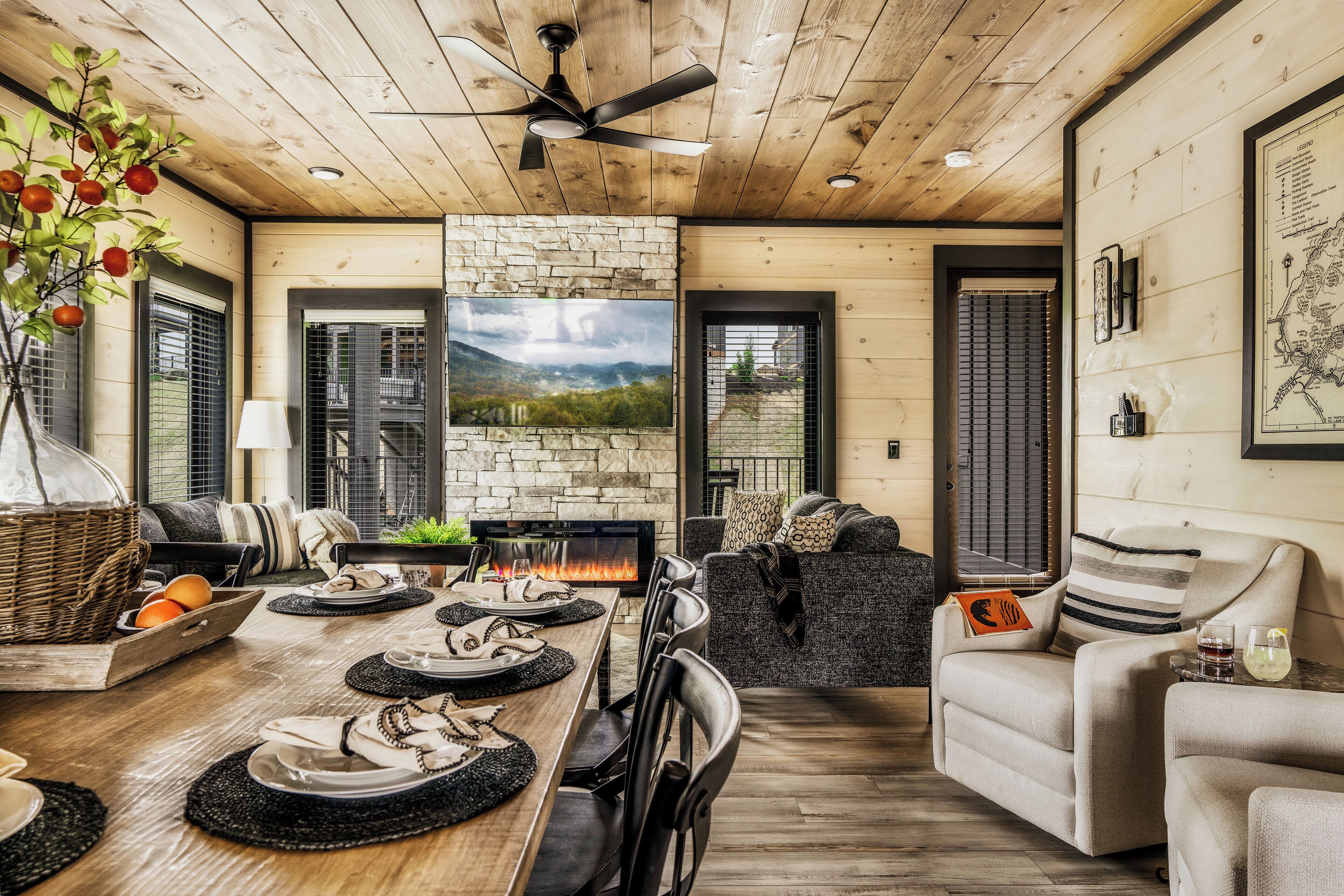 A dining area with a wooden table set for four, a stone fireplace, and a view of the outdoors through a window.