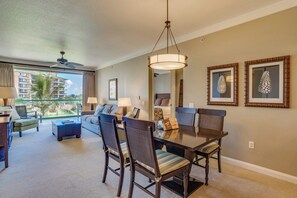 Une chambre d’hôtel avec un balcon, un coin repas avec une table et des chaises, un canapé et un ventilateur de plafond.