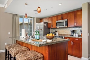 A modern kitchen with wooden cabinets, stainless steel appliances, a large island with seating, and pendant lighting.