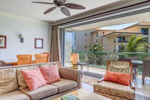 Habitación de hotel con balcón, ventilador de techo, sofá, sillón y mesa.