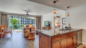 A modern hotel room with a kitchen island, dining area, and a balcony with a view of the city. - Honua Kai | Ocean View 4 BR, Sleeps 12 | Car Incl. w/ 6+ Nights | HKH ML-1793 by KBM (Lahaina)