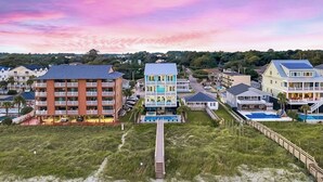 Et kysthotel med flere bygninger, en strand i forgrunden og en træbro, der fører til stranden.