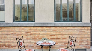 A small outdoor table with two chairs, set against a brick wall with windows above. - Sublim Apartement Center of Paris (Paris)