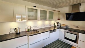 A modern kitchen with white cabinets, a black countertop, a stainless steel kettle, a coffee maker, and a built-in oven. - Charming country house with garden - lakes & foothills of the Alps (Penzberg)