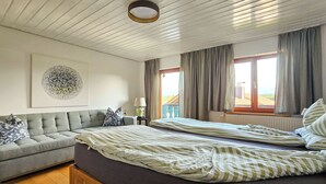 A bedroom with a bed, a sofa, a lamp, and a window with curtains. - Charming country house with garden - lakes & foothills of the Alps (Penzberg)