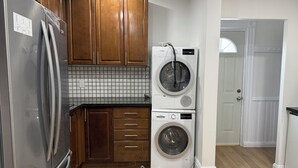 Ett kök med träskåp, ett kylskåp i rostfritt stål, en tvättmaskin från Bosch och en kakelbeklädd vägg bakom diskbänken.