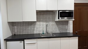 Ett kompakt kök med vita skåp, en diskho i rostfritt stål, en mikrovågsugn och ett kaklat stänkskydd.