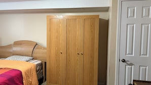 A bedroom with a wooden wardrobe, a bed with a headboard, and a door.