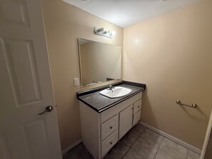 Un baño con lavamanos blanco, un espejo, una puerta y un perchero para toallas.