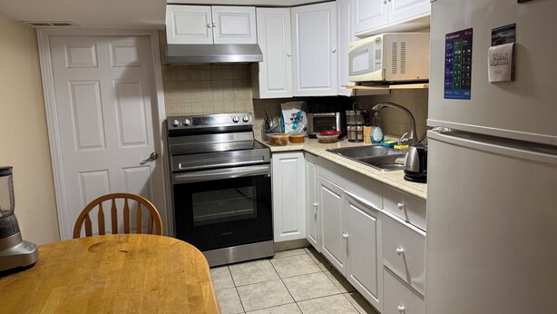 A compact kitchen with white cabinets, a stainless steel oven, a microwave, and a refrigerator.