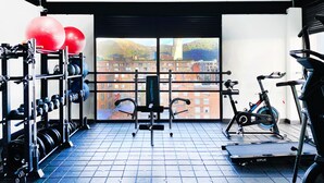 Un gimnasio con equipo de ejercicio, una ventana con vista a la ciudad y suelo de baldosas.
