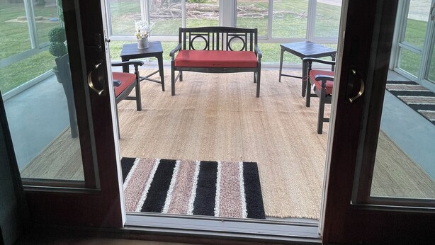 Une porte vitrée donne sur un patio extérieur aménagé avec un banc, deux tables et un tapis.