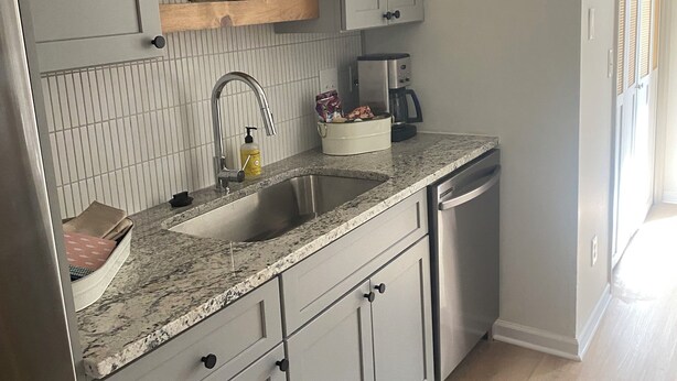 A modern kitchen with grey cabinetry, a granite countertop, a stainless steel sink, and a coffee maker.