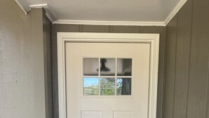 A white front door with a small window above it, a doorbell, and a black doormat.