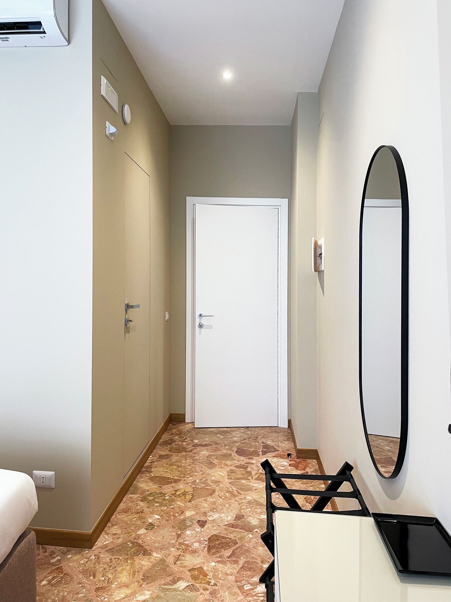 Ein Hotelkorridor mit Marmorboden, einer weißen Tür, einem Spiegel und einer kleinen Sitzecke mit Tisch und Stühlen.