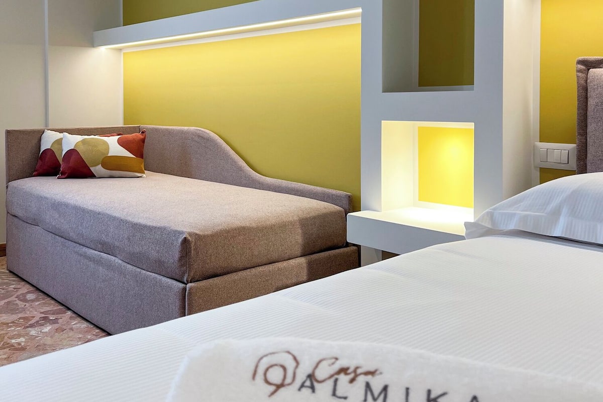 A modern hotel room with a sofa, a bed, and a nightstand.