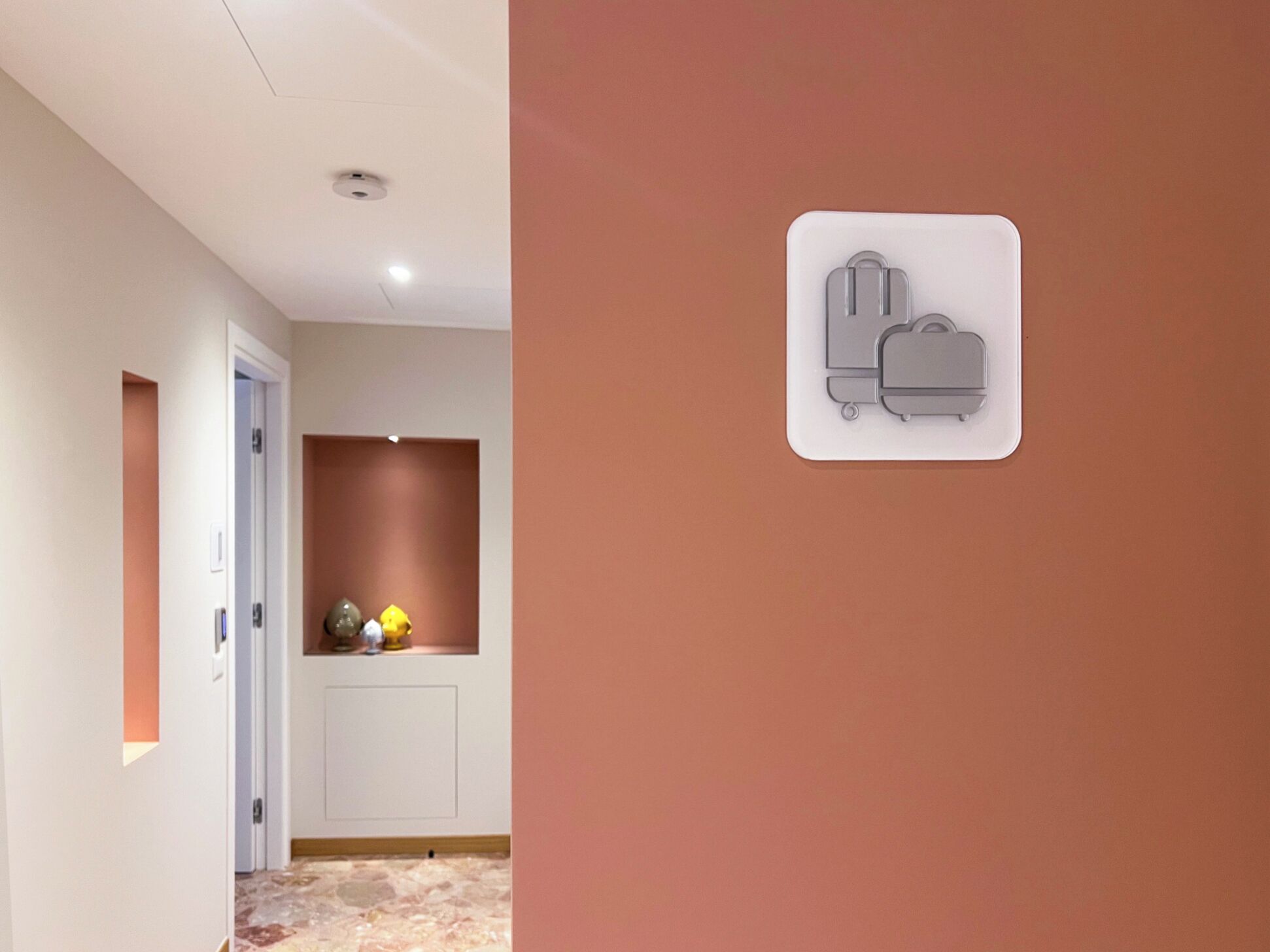 Un couloir avec une porte blanche, un mur marron et une petite étagère ornée d’objets décoratifs.
