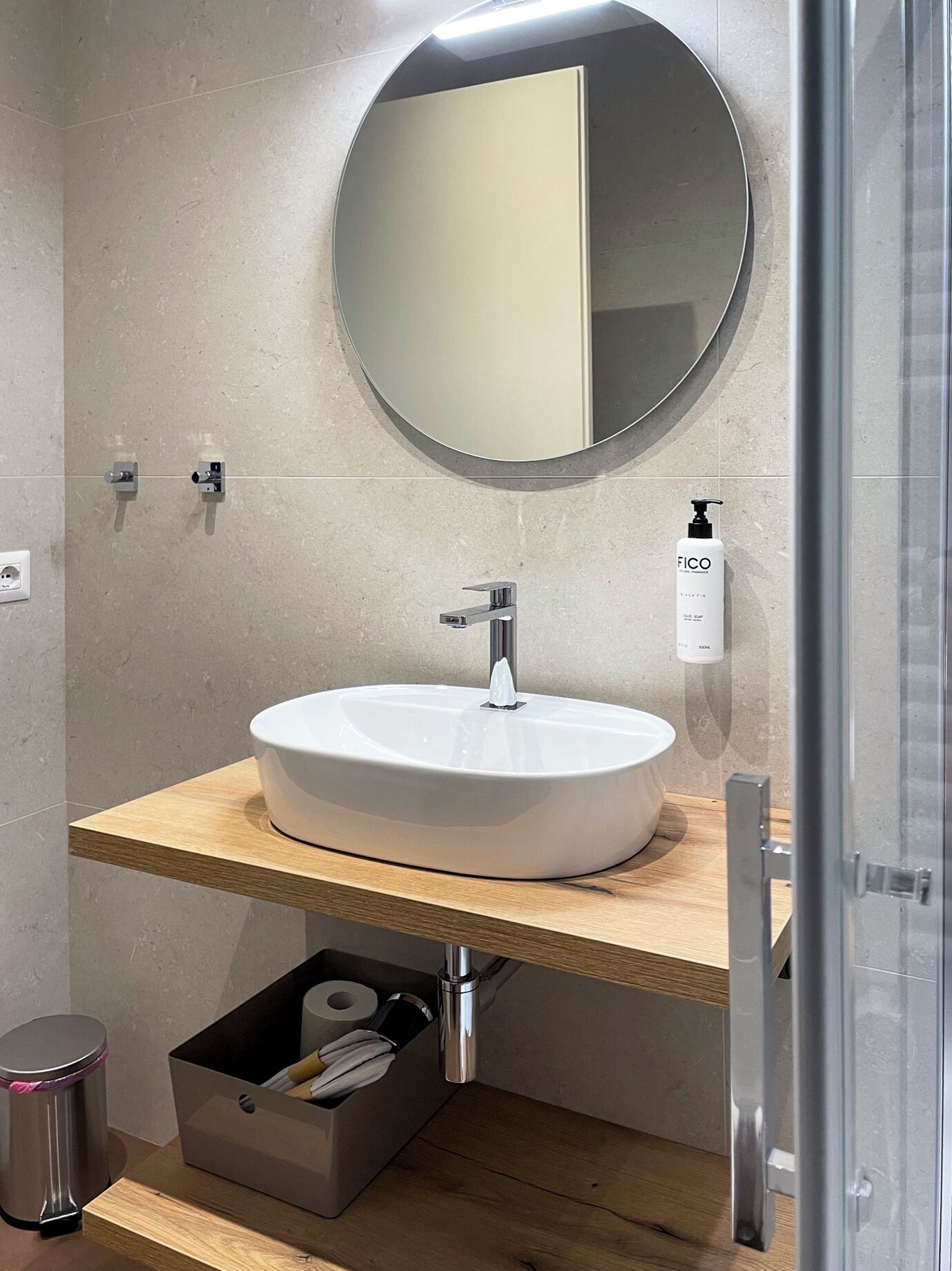 A bathroom with a round mirror, a white sink, and a wooden countertop.