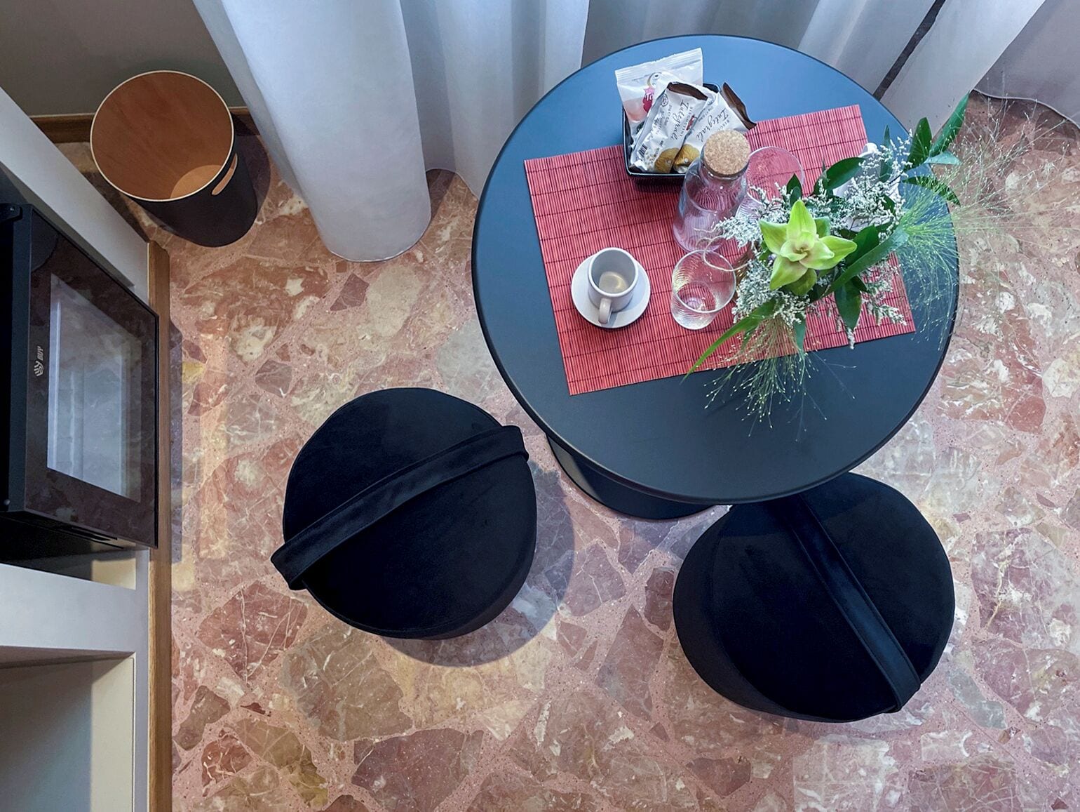 A small round table with a red placemat, two black stools, a small tray with snacks, a glass jar, and a decorative plant.