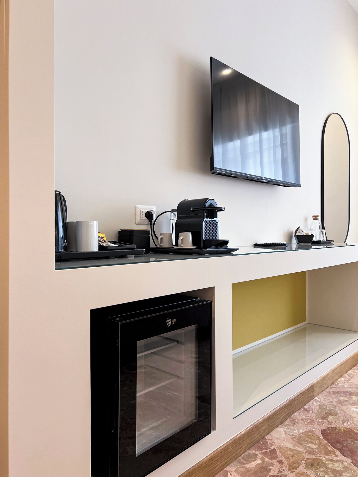 A modern kitchen with a built-in oven, a coffee machine, and a flat-screen TV mounted on the wall.