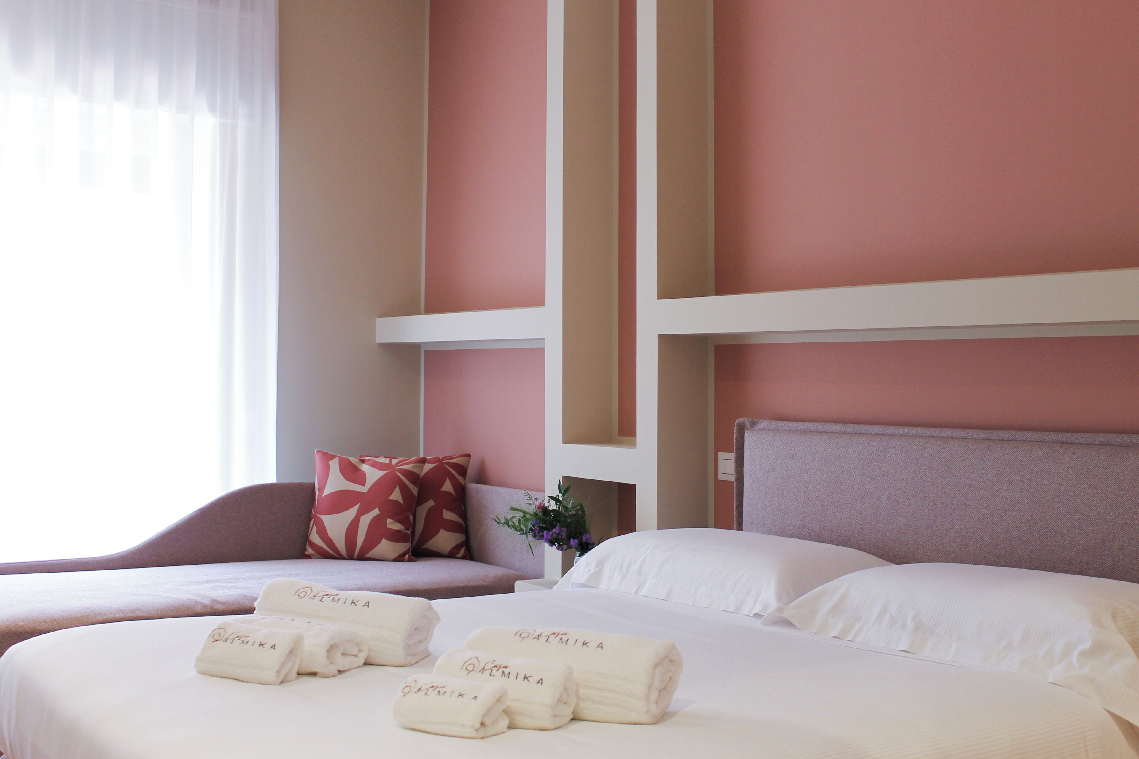 A hotel room with two beds, a sofa, and a window with sheer curtains.