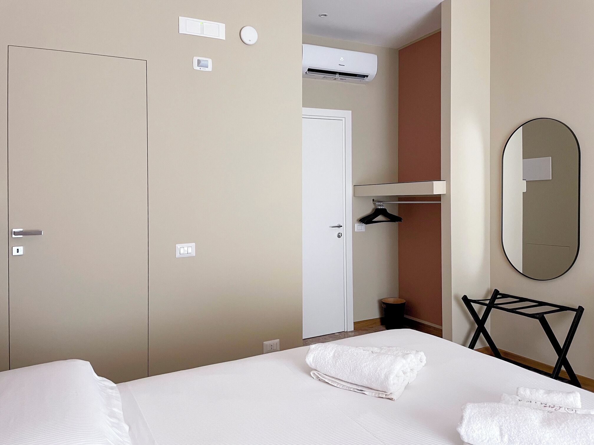 A hotel room with a bed, a white towel, a hanging towel rack, a mirror, and a door.