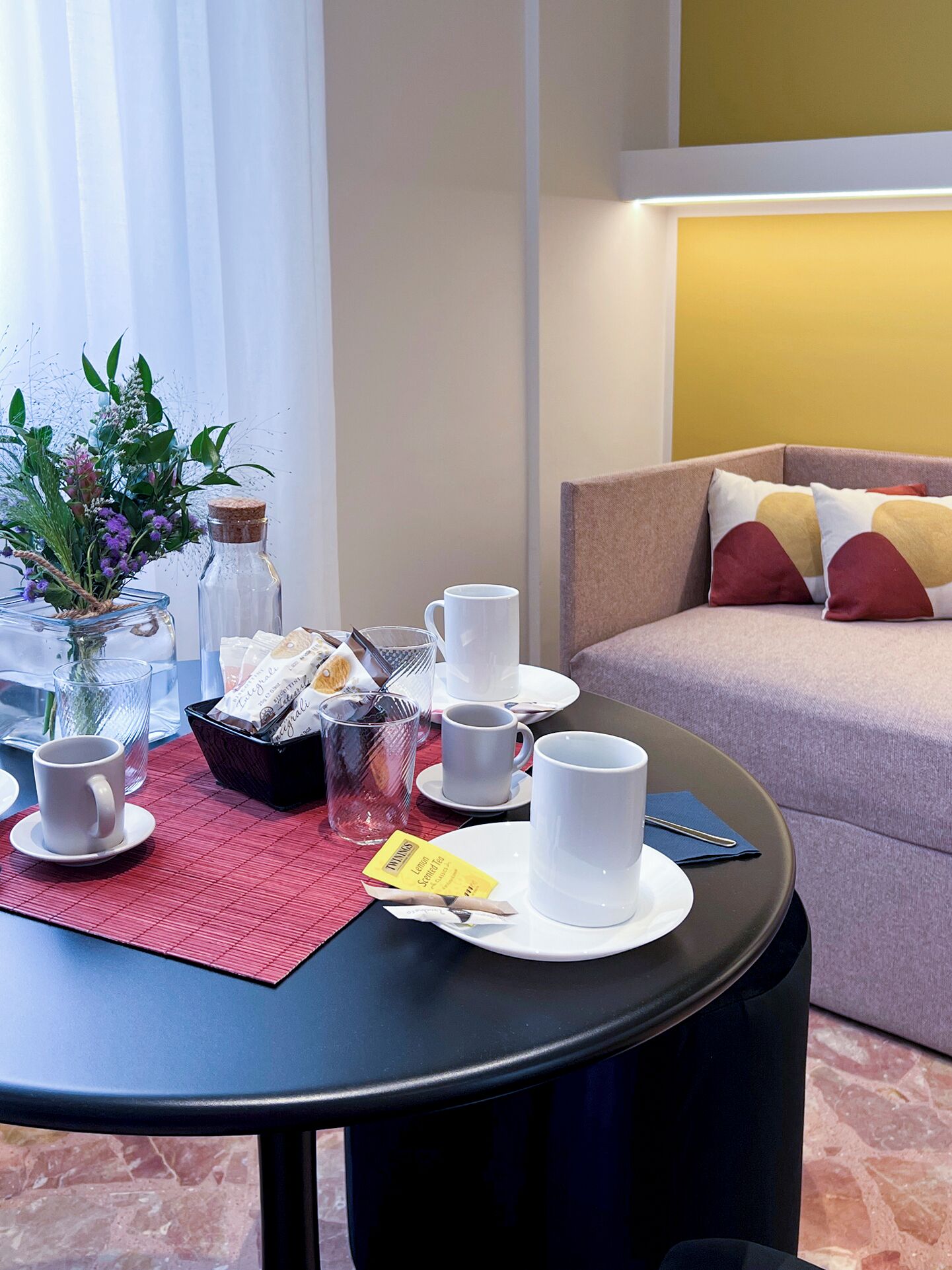 A neatly arranged breakfast table with cups, a tea packet, and a vase with flowers.