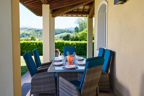 An outdoor dining area with a table set for four, surrounded by wicker chairs with blue cushions, under a wooden pergola.