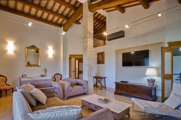 A spacious living area with a high ceiling, a television mounted on the wall, and a comfortable seating arrangement including sofas and a bench.