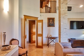 A spacious living area with a high ceiling, a wooden staircase, a painting, and a flat-screen TV mounted on the wall.