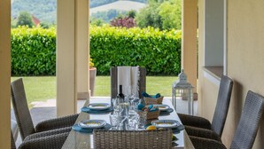 A dining table set for six with wicker chairs, a view of a green landscape, and a white lantern on the table.