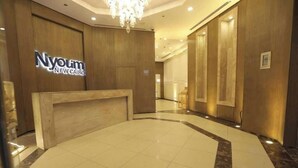 A hotel reception area with a wooden reception desk, a chandelier, and a sign that reads "Nyouim New Cairo".